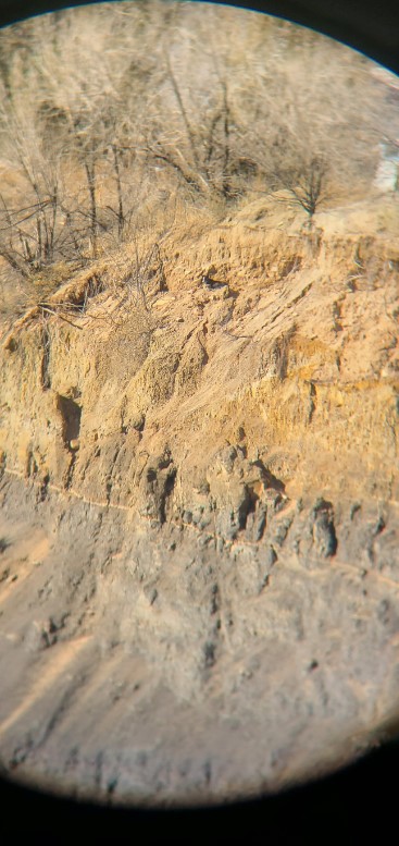 a man looks through binoculars at a cliff