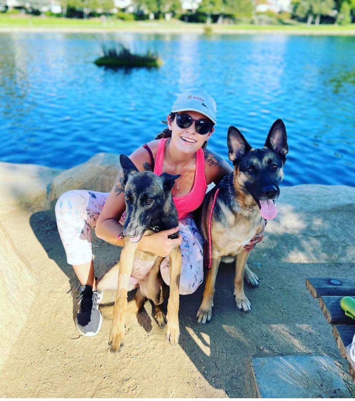 smiling woman posing with two dogs by the lake